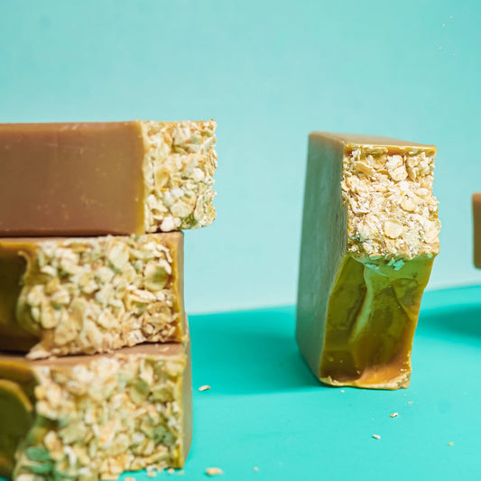 Artisan oatmeal soap bars with textured oats on top, displayed on a turquoise background.