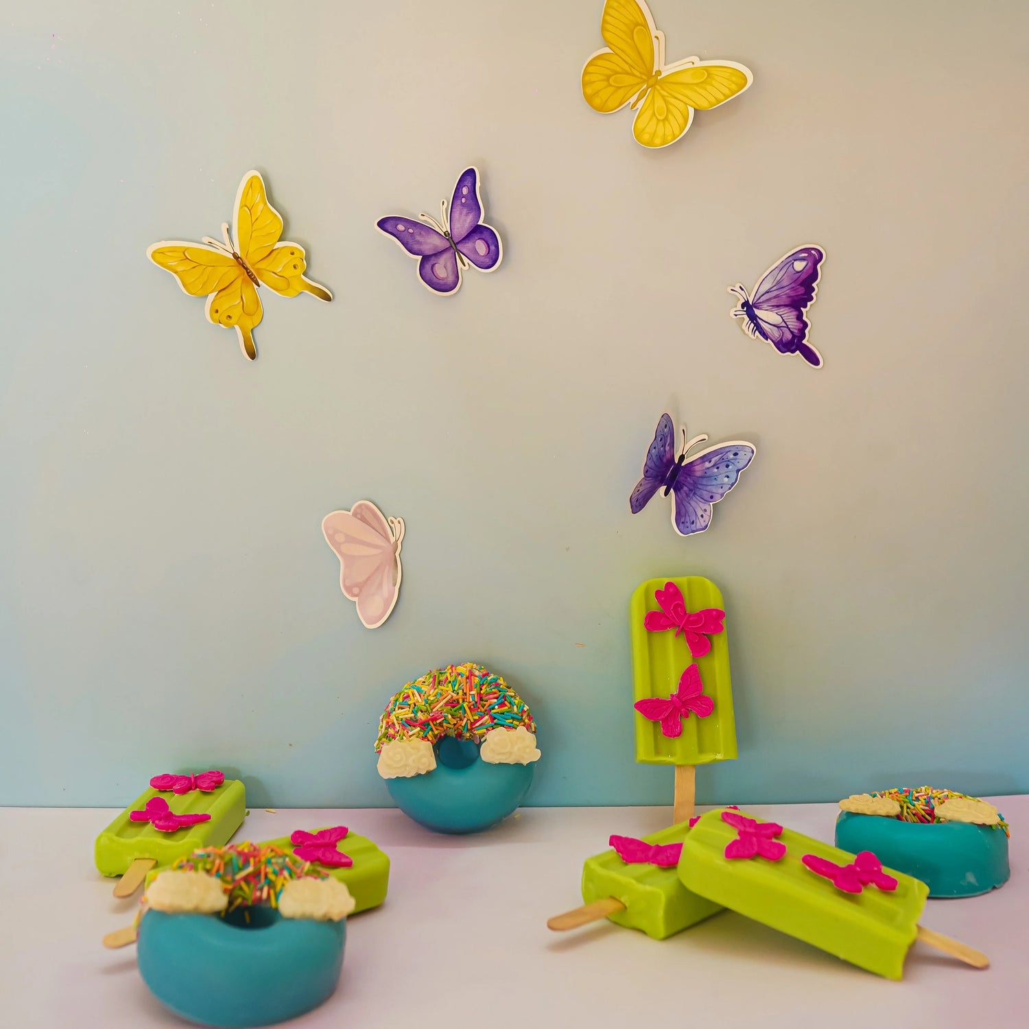 Colorful bath treats shaped like donuts and popsicles with butterfly decorations and rainbow sprinkles.