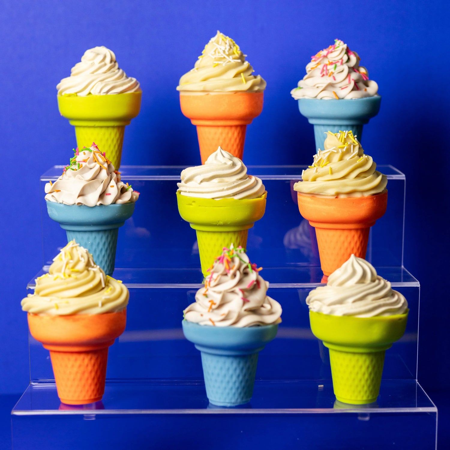 Colorful cone-shaped artisan soap cupcakes with whipped tops and sprinkles on acrylic display